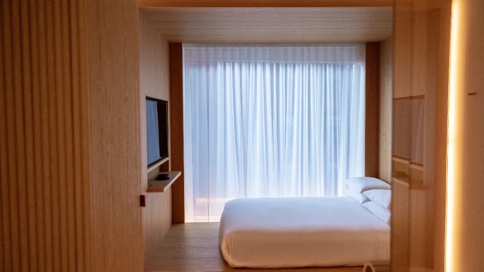 Chambre d’hôtel avec lit fait, rideaux clairs et boiseries chaudes