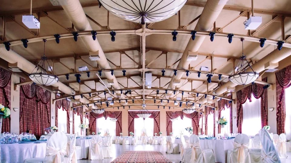 Salle de réception dressée pour un événement, tables rondes et draperies